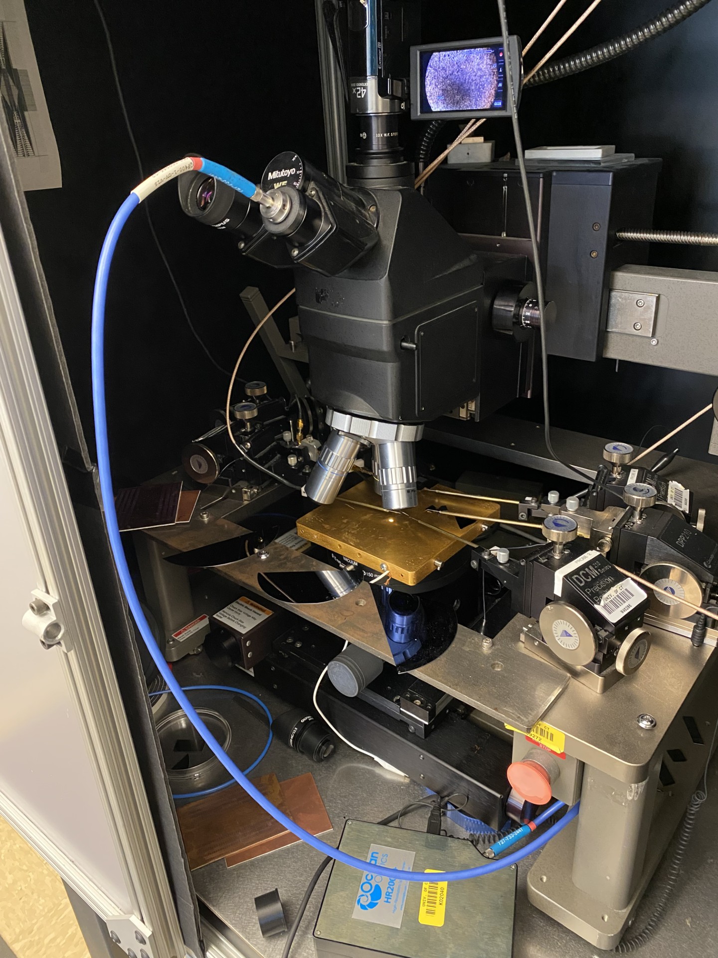 The full measurement rig: Mitutoyo microscope with blue OceanOptics HR2000+ fiber cable routing into the eyepiece tube, gold wafer stage below the objective, and DCM motorized stage to the right.